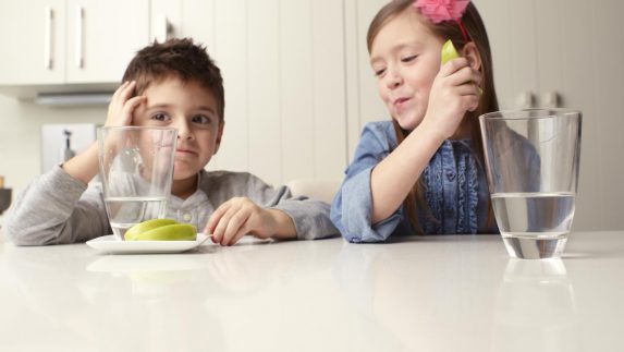 Boy and girl sit at a table with apple slices and water