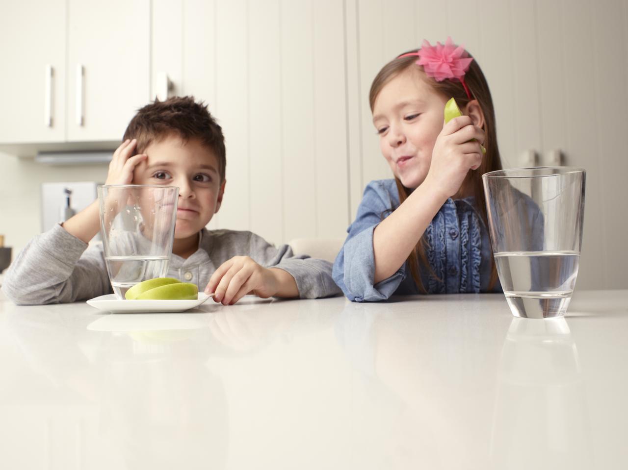 Boy and girl sit at a table with apple slices and water