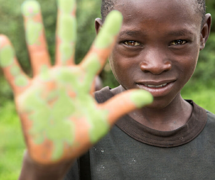 Zambian boy holding up his left hand painted green during a Nutrilite Little Bits distribution event.