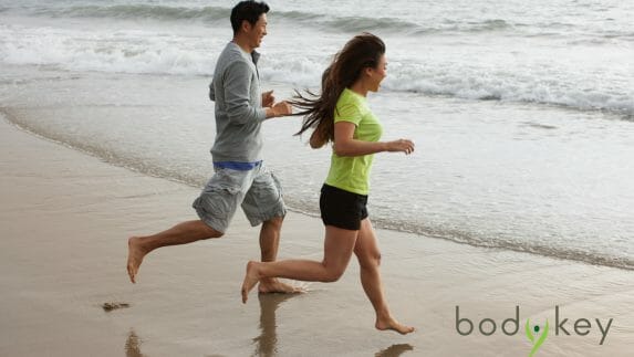 Man and woman running on a beach towards the water