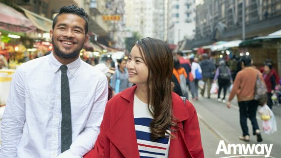 A man and a woman hold hands while walking in a busy city