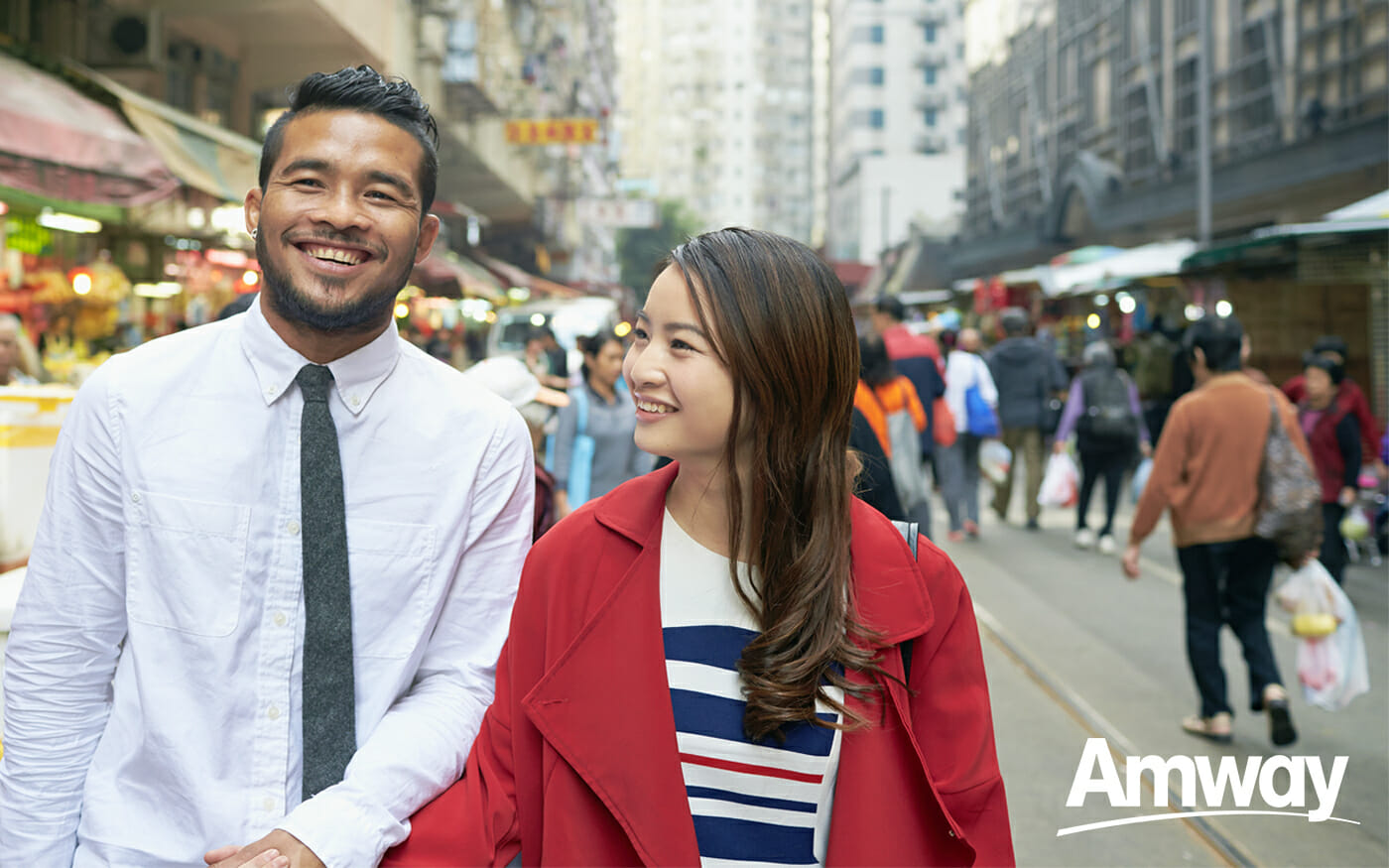 A man and a woman hold hands while walking in a busy city