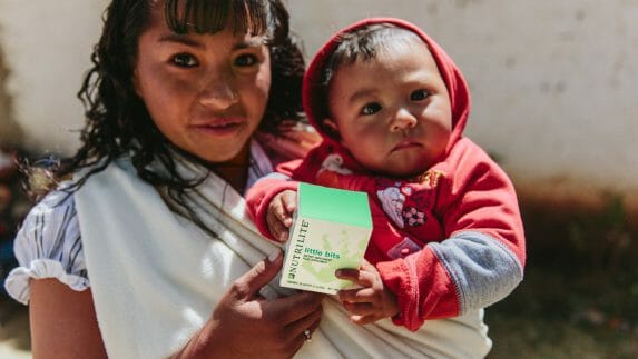 Woman holding a child with a bottle of Nutrilite Little Bits