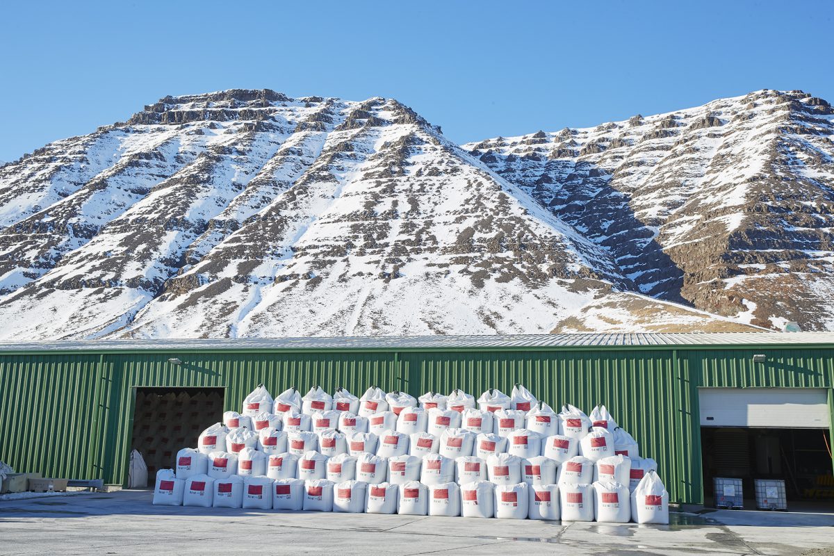 Large bags stacked on top of each other outside a warehouse with mountains in the background.