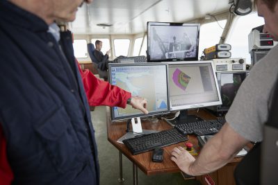 Men working aboard a harvesting ship using a computer
