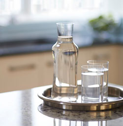 A glass bottle and two glass cups of water on a silver tray