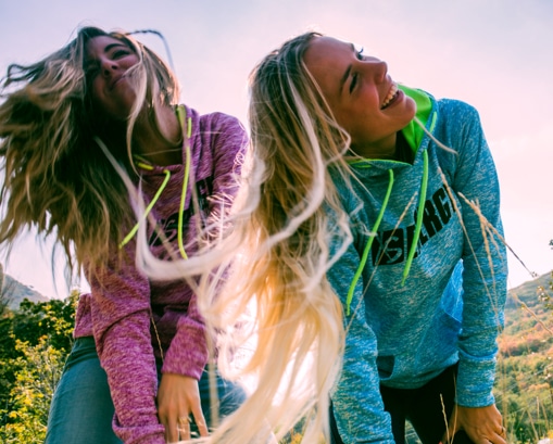 Two women being active outdoors with their hair hanging down towards the camera