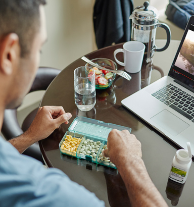 Lifestyle image showing a man sitting at a table with a laptop, Nutrilite Double X, vitamin B, a serving of fruit salad and coffee in a French press. Breakfast provides nutrients we need for energy so we can focus and perform throughout the day.