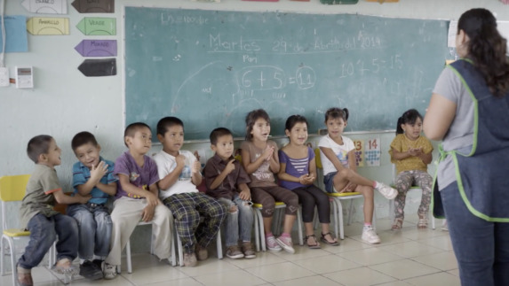 A teacher stands before a group of young students who are seated by a chalkboard. Through our One by One Campaign for children, Amway builds partnerships with organizations that address issues specific to children in their communities.