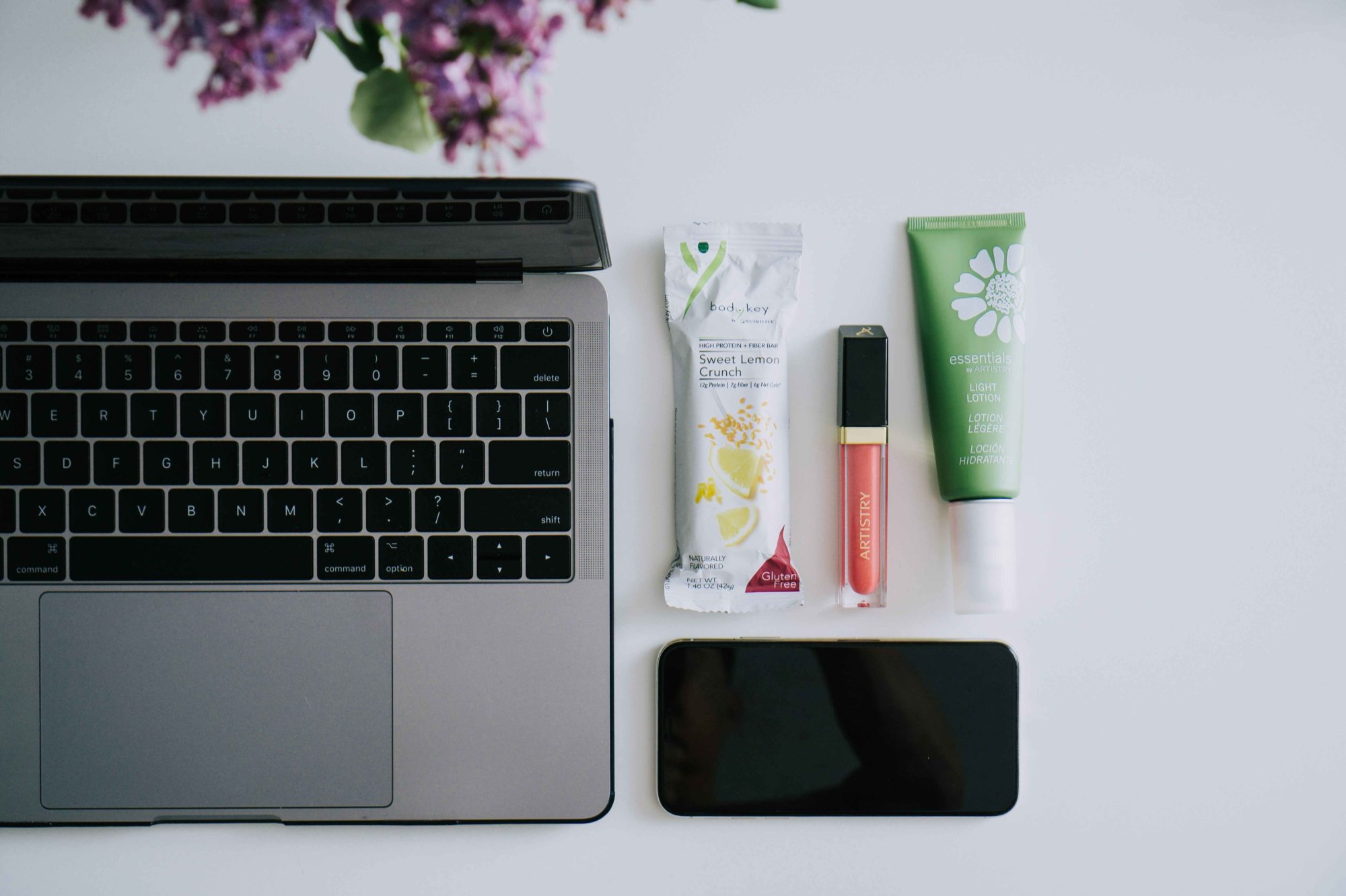 Flat lay with Sweet Lemon Crunch BodyKey bar, Artistry Light Up Lip Gloss, Artistry essentials Light Lotion near an open laptop and a smart phone. This image is from one of the monthly downloadable packages of photos for our business owners to use on social media, whether that’s WeChat or Facebook, Instagram or Line.