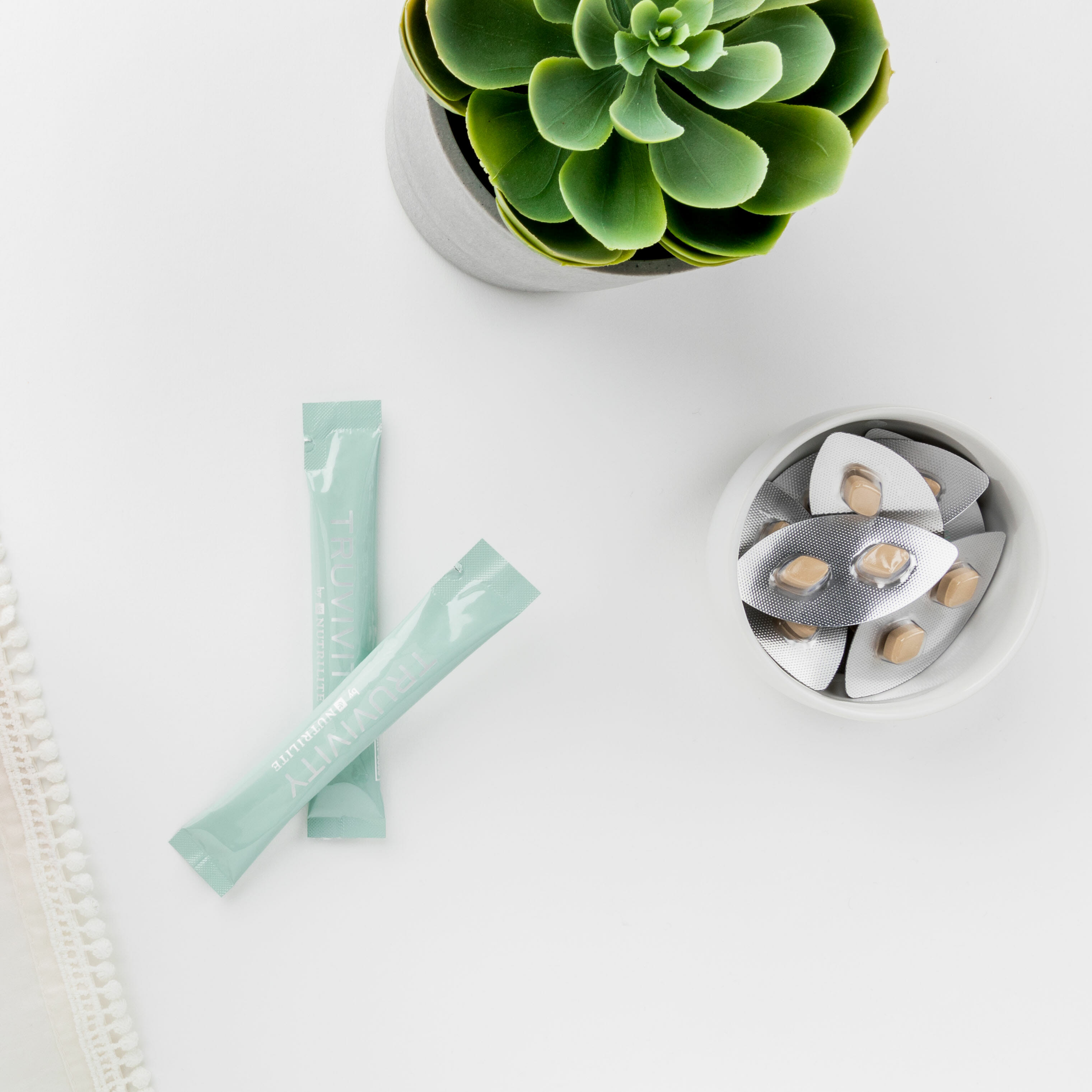 A tabletop with a succulent next to Truvivity powder drink stick packs and supplements. Truvivity is a simple yet powerful way to balance the sugars in your body and prevent the breakdown of skin cells leading to skin damage.