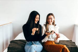 2 young women sitting on the foot of a bed sharing Artistry makeup products