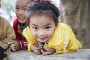 Asian toddler girl leaning over a table and smiling