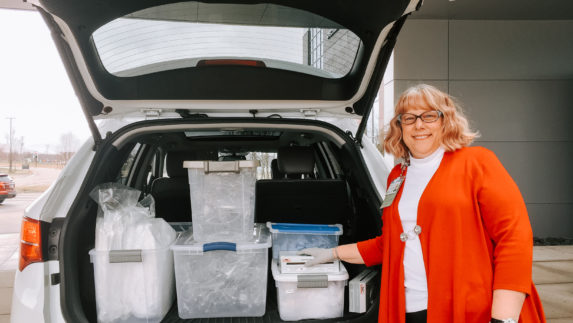 Amway employee standing next to plastic bins of personal protective equipment in the back of an SUV