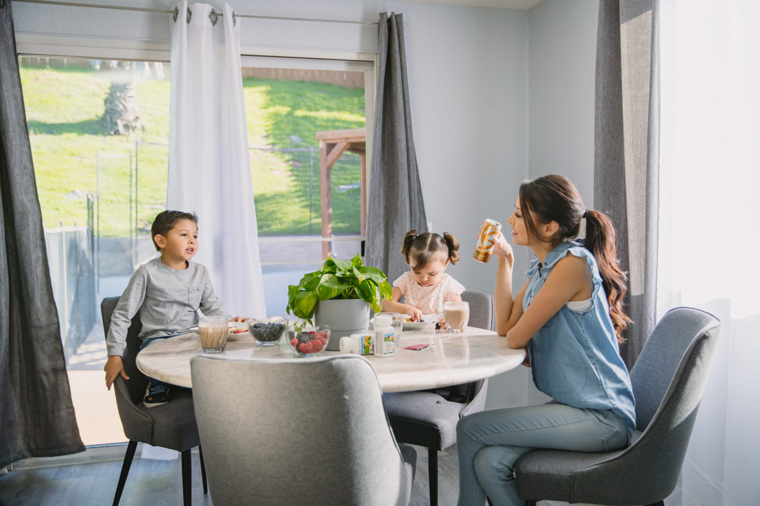 Woman drinking an XS energy drink while sitting at the table with her two children