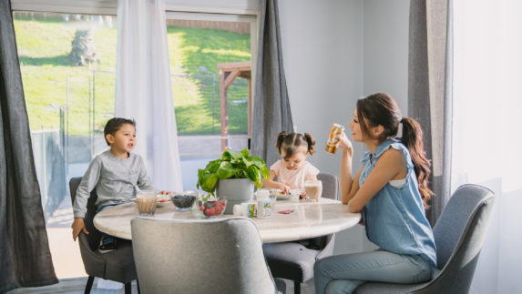 Woman drinking an XS energy drink while sitting at the table with her two children