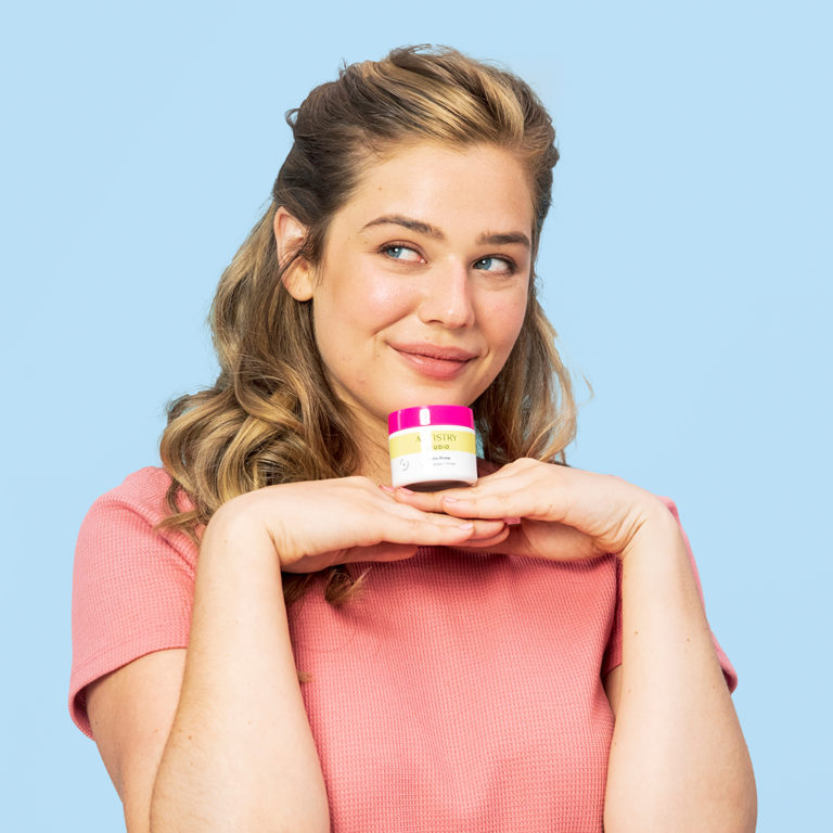 Girl smiling with an artistry studio products jar sitting on top of her hands under her face while she looks to her right