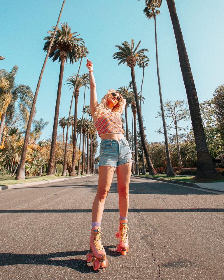 Woman in roller skates in the middle of the street lined with palm trees