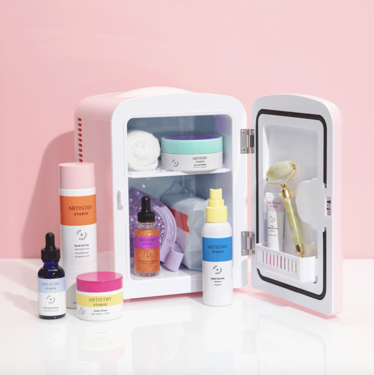 Skincare fridge sitting in front of a pink backdrop filled with all types of artistry products and accessories