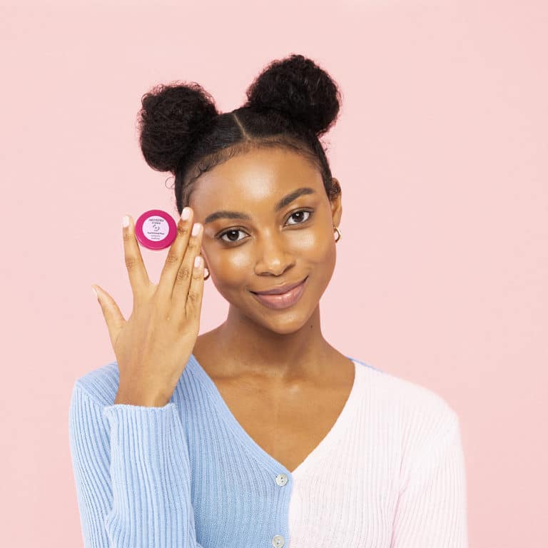 Woman standing in front of a pink backdrop holding an artistry product next to her face