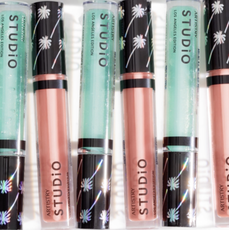 Six tubes of artistry studio LA edition lip glosses laying together half blush and half teal colored