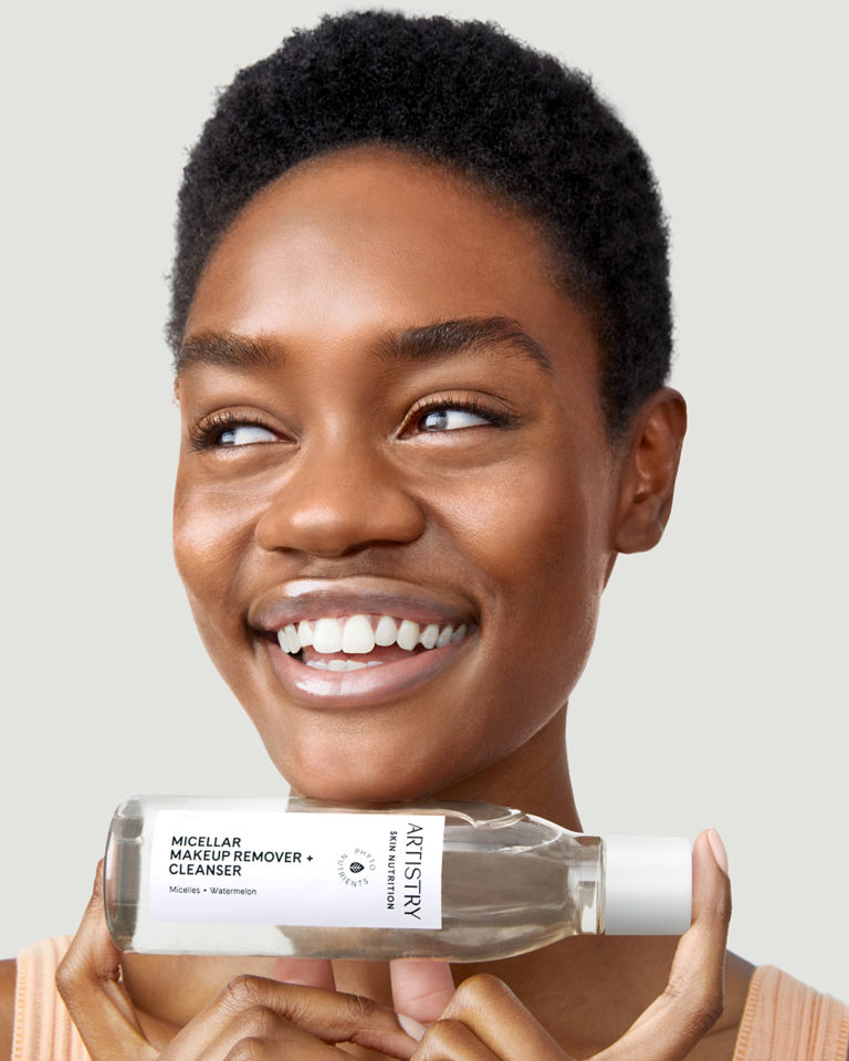 Woman smiling looking to her right holding a bottle of Artistry micellar makeup remover and cleanser under her face