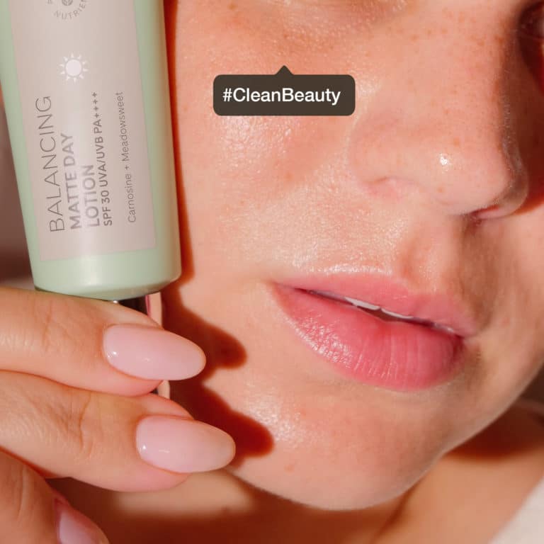 Close up of an eyeless woman holding the balancing matte day lotion SPF 30 up to her face. With the tag #CleanBeauty